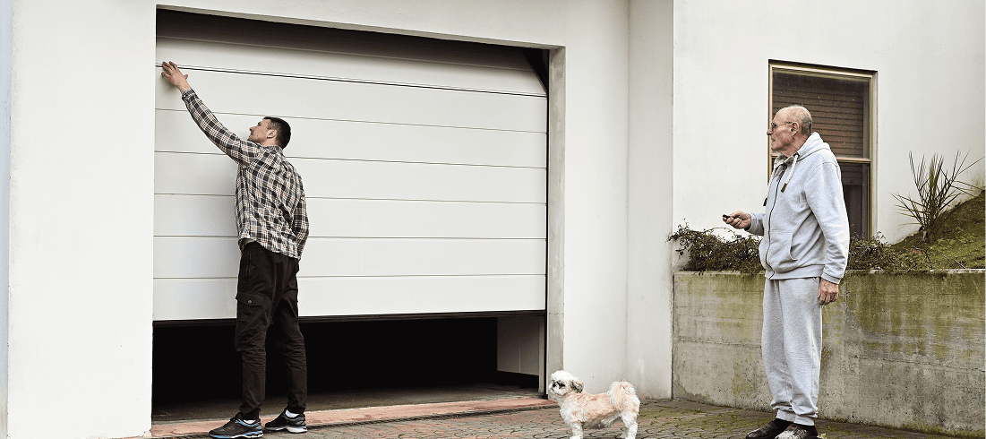 Two men and dog outside opening garage.