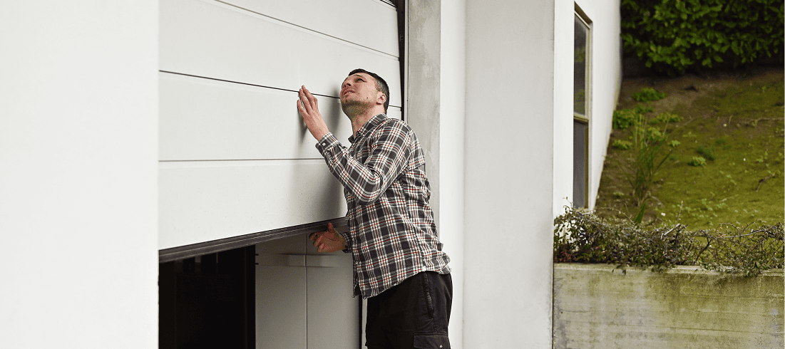 Man inspecting a partially open garage door.