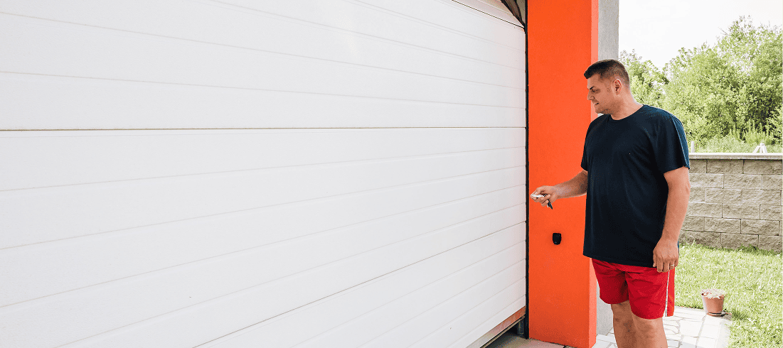 Man opening white garage door with remote.